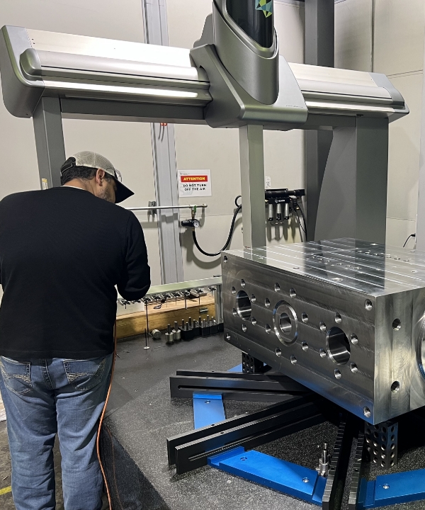 Operator performing CMM inspection on a metal component in a laboratory setting.